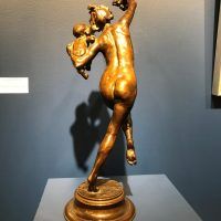 Bronze sculpture of a woman holding fruit in the air in one hand, and a baby in the other