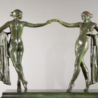 Alt text: Bronze sculpture of two classical women looking at each other holding drapery in one arm and extending the other to hold hands