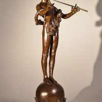 Alt text: Bronze fountain sculpture of the deity Pan mischeviously playing two flutes, standing atop a sphere flanked by fish, angled view