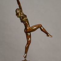 Alt text: Bronze sculpture of a nude woman posing with arms outstretched in an L shape and right leg lifted with knee bent