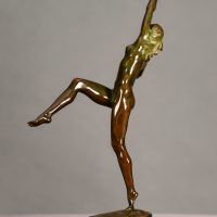 Alt text: Bronze sculpture of a nude woman posing with arms outstretched in an L shape and right leg lifted with knee bent