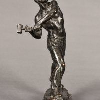 Alt text: Bronze sculpture of a muscular shirtless man swinging a hammer