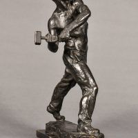 Alt text: Bronze sculpture of a muscular shirtless man swinging a hammer