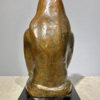 Alt text: Bronze sculpture of a girl with crossed arms, rear view