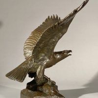 Alt text: Bronze sculpture of eagle preparing to take flight off a rocky point, angled view 