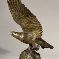 Alt text: Bronze sculpture of eagle preparing to take flight off a rocky point, angled view 