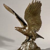 Alt text: Bronze sculpture of eagle preparing to take flight off a rocky point, angled view 