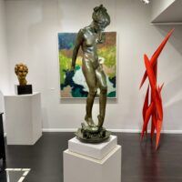 Alt text: Bronze sculpture of a young nude woman standing among frogs, gallery installation view