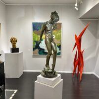 Alt text: Bronze sculpture of a young nude woman standing among frogs, gallery installation view