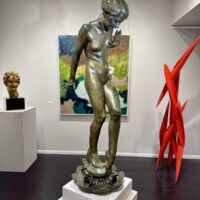 Alt text: Bronze sculpture of a young nude woman standing among frogs, gallery installation view