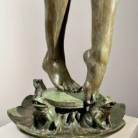 Alt text: Bronze sculpture, detail of two feet among frogs