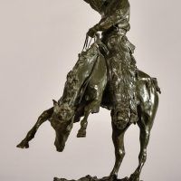 Alt text: Bronze sculpture of a rearing bronco with a cowboy on his back, holding his hat off his head with his right hand