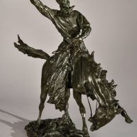 Alt text: Bronze sculpture of a rearing bronco with a cowboy on his back, holding his hat off his head with his right hand