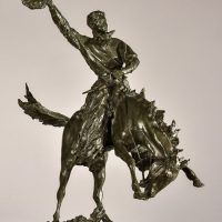 Alt text: Bronze sculpture of a rearing bronco with a cowboy on his back, holding his hat off his head with his right hand