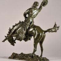 Alt text: Bronze sculpture of a rearing bronco with a cowboy on his back, holding his hat off his head with his right hand