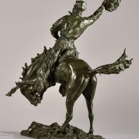 Alt text: Bronze sculpture of a rearing bronco with a cowboy on his back, holding his hat off his head with his right hand