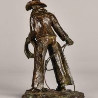 Alt text: Bronze sculpture of a standing cowboy with lasso, angled view