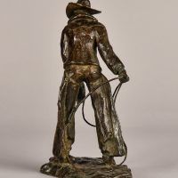 Alt text: Bronze sculpture of a standing cowboy with lasso, angled view