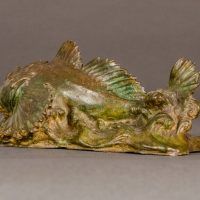 Alt text: Bronze sculpture of a sculpin fish atop the water, angled view
