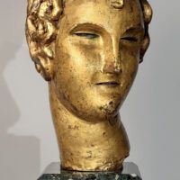 Alt text: Stylized, gilt bronze sculpture of a head of a boy with curly hair