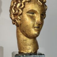 Alt text: Stylized, gilt bronze sculpture of a head of a boy with curly hair