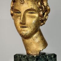 Alt text: Stylized, gilt bronze sculpture of a head of a boy with curly hair