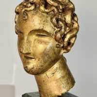 Alt text: Stylized, gilt bronze sculpture of a head of a boy with curly hair