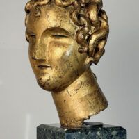Alt text: Stylized, gilt bronze sculpture of a head of a boy with curly hair