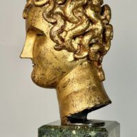 Alt text: Stylized, gilt bronze sculpture of a head of a boy with curly hair