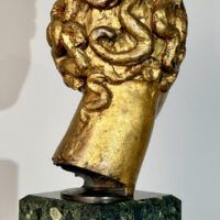 Alt text: Stylized, gilt bronze sculpture of a head of a boy with curly hair