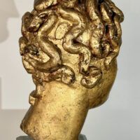 Alt text: Stylized, gilt bronze sculpture of a head of a boy with curly hair