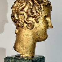 Alt text: Stylized, gilt bronze sculpture of a head of a boy with curly hair