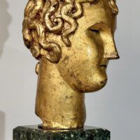 Alt text: Stylized, gilt bronze sculpture of a head of a boy with curly hair