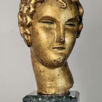 Alt text: Stylized, gilt bronze sculpture of a head of a boy with curly hair