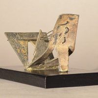 Alt text: Abstract soldered lead sculpture atop a wooden base resembling a drawbridge, angled view