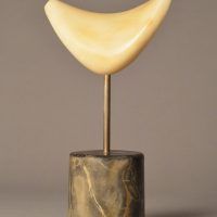 Alt text: Boomerang-shaped marble sculpture mounted on marble, attached by a short metal poll, frontal view