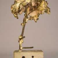 Alt text: Welded bronze sculpture shaped like a tree mounted on a slag block, side view