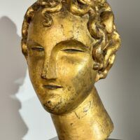 Alt text: Gilt bronze sculpture of a head of a boy with curly hair