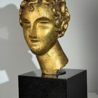 Alt text: Gilt bronze sculpture of a head of a boy with curly hair