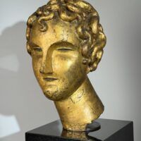 Alt text: Gilt bronze sculpture of a head of a boy with curly hair