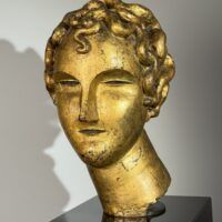 Alt text: Gilt bronze sculpture of a head of a boy with curly hair