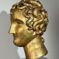 Alt text: Gilt bronze sculpture of a head of a boy with curly hair