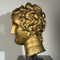 Alt text: Gilt bronze sculpture of a head of a boy with curly hair