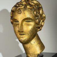 Alt text: Gilt bronze sculpture of a head of a boy with curly hair