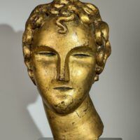 Alt text: Gilt bronze sculpture of a head of a boy with curly hair