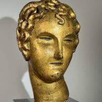 Alt text: Gilt bronze sculpture of a head of a boy with curly hair