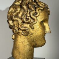 Alt text: Gilt bronze sculpture of a head of a boy with curly hair