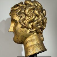 Alt text: Gilt bronze sculpture of a head of a boy with curly hair