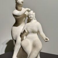 Alt text: White sculpture of two women, one standing and one seated
