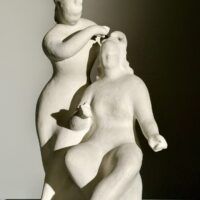 Alt text: Stylized, white sculpture of two women, one standing and one seated